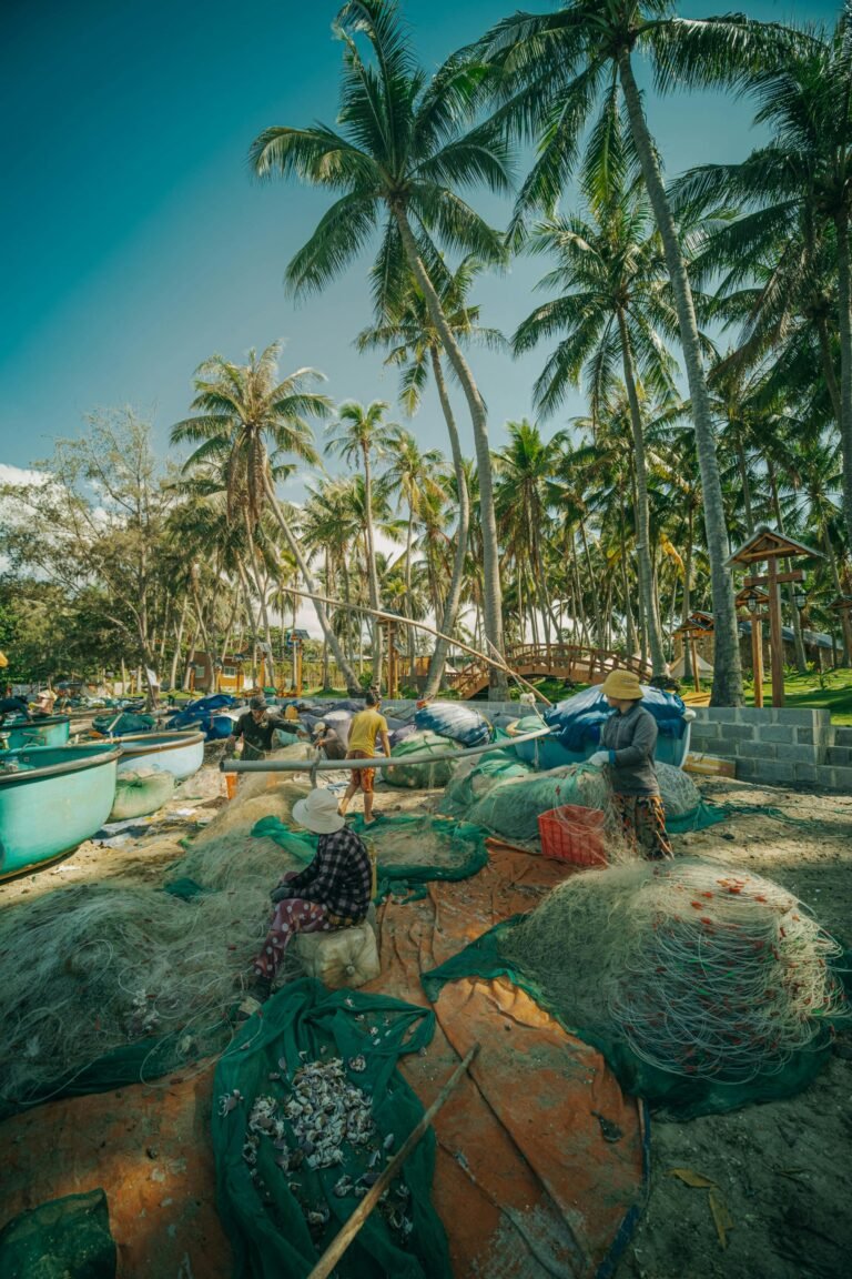 Fishermen repairing nets by boats amidst palm trees in a tropical setting.