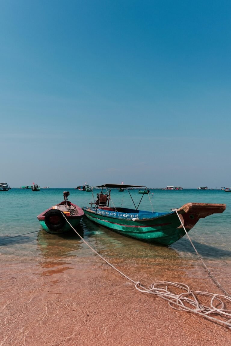 Traditional wooden boats docked on the tranquil shores of Phu Quoc, Vietnam under a clear blue sky.